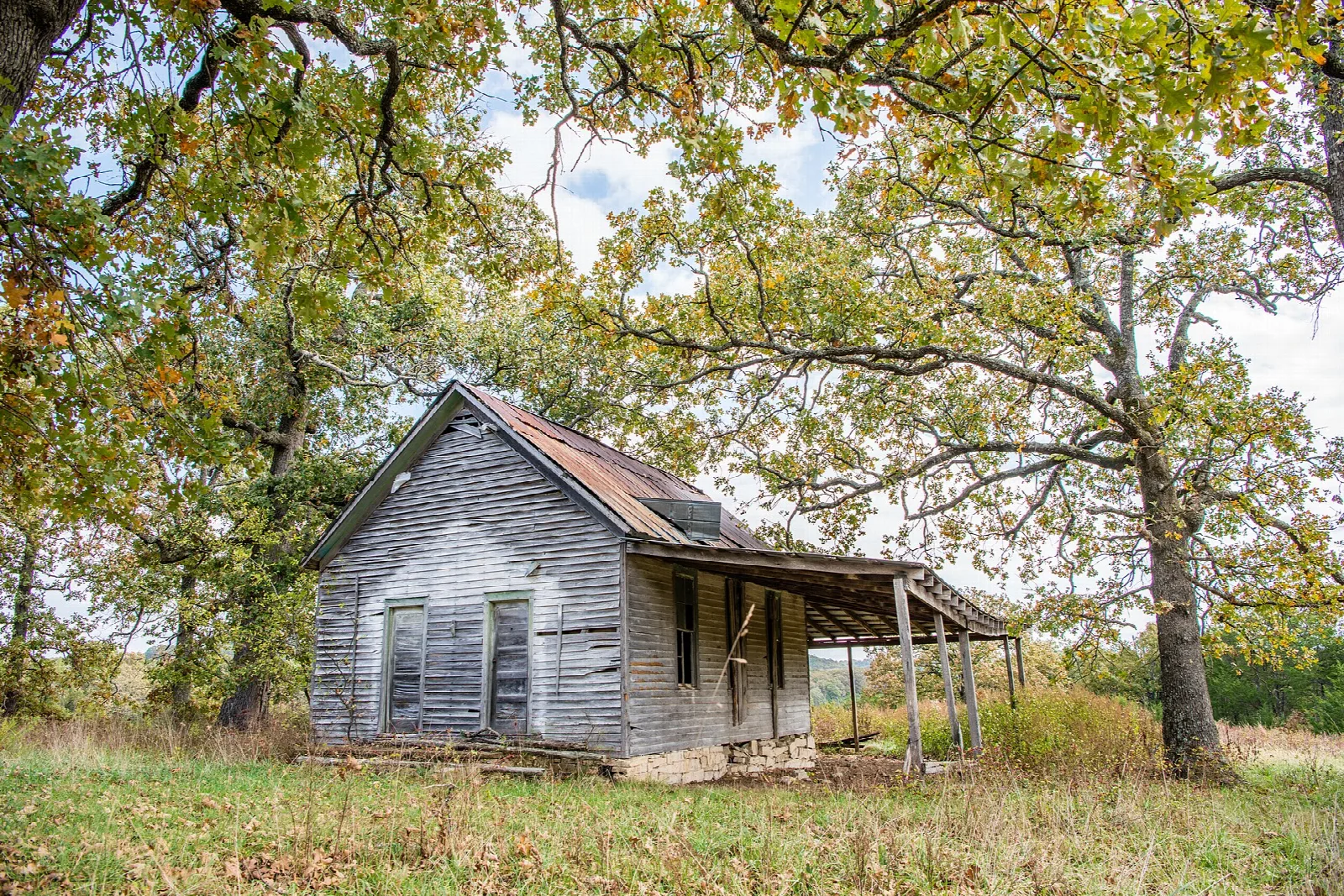 Old weathered wooden house with a porch under large oak trees