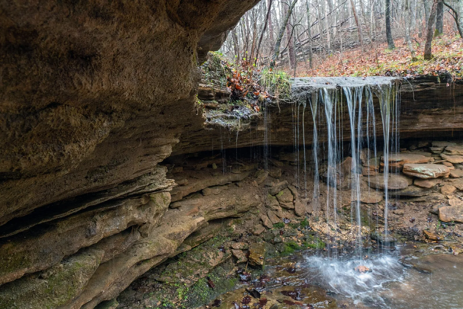 Small waterfall dripping over a rock overhang into a pool