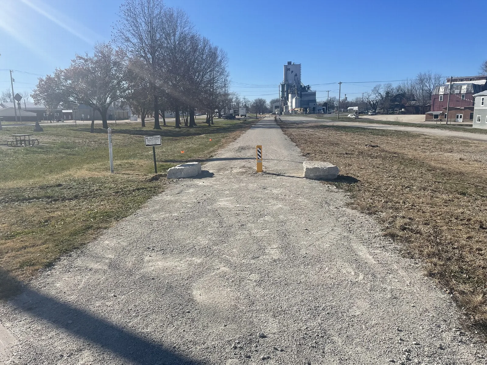 Wide gravel trail leading toward a grain elevator in a small town