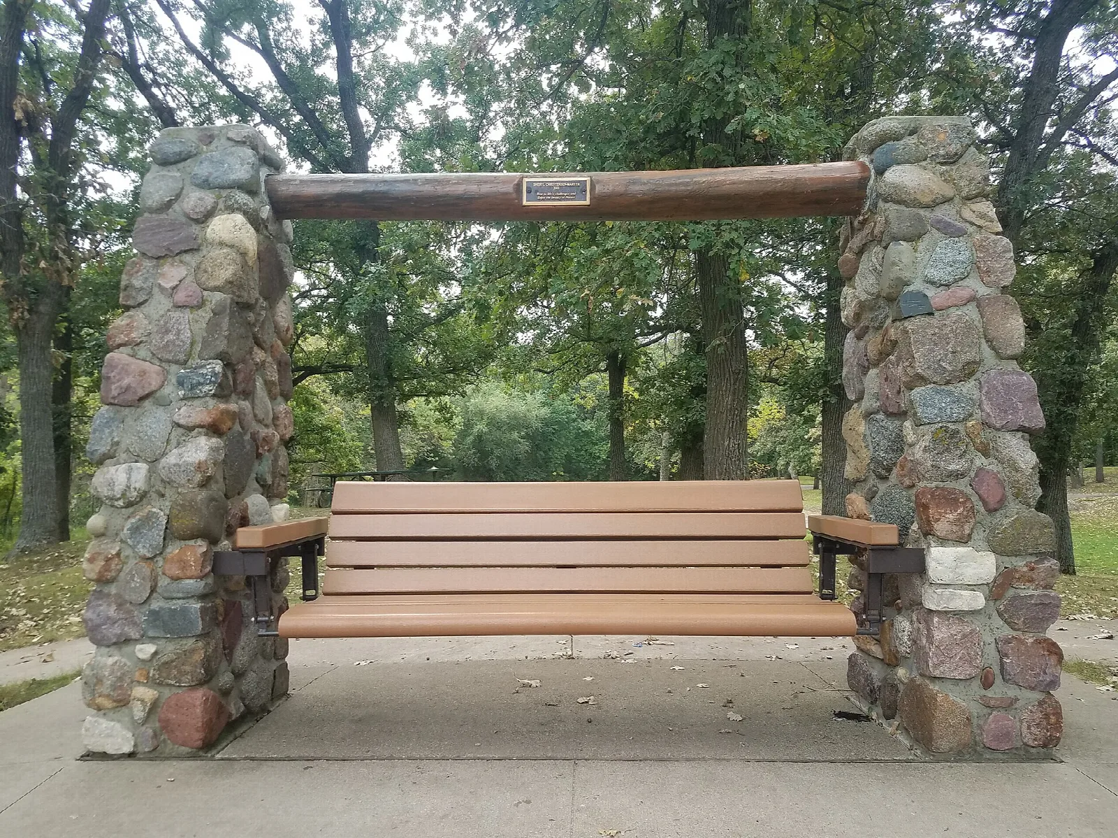 Wooden bench swing between two fieldstone pillars under tall trees