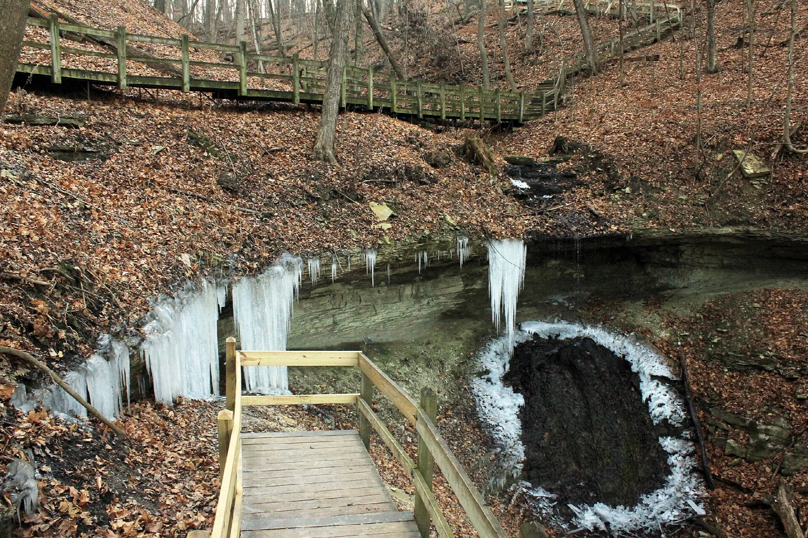 Frozen waterfall with icicles beside a wooden boardwalk staircase in winter woods