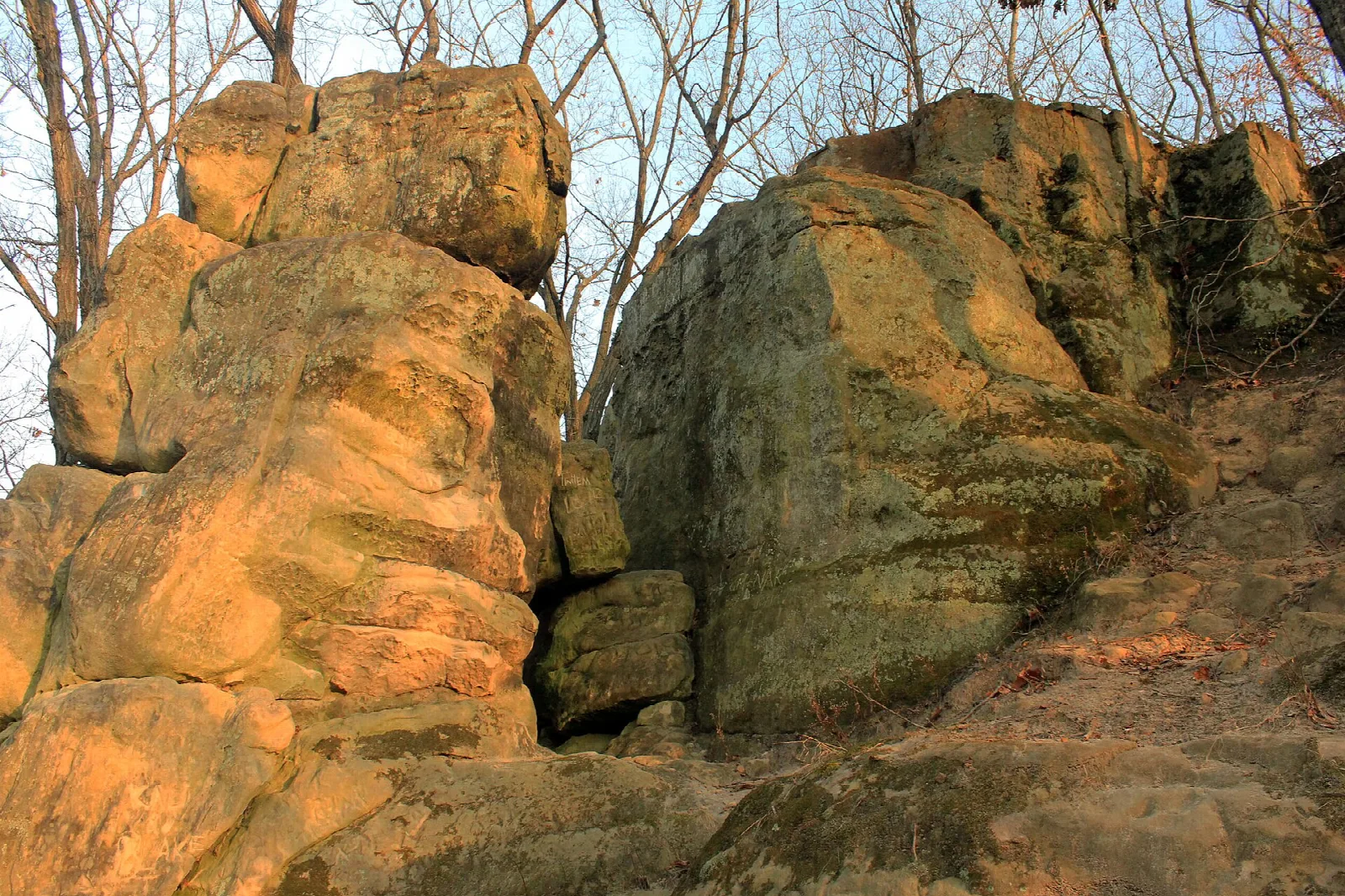Large sunlit sandstone rock formations beside a trail among bare trees