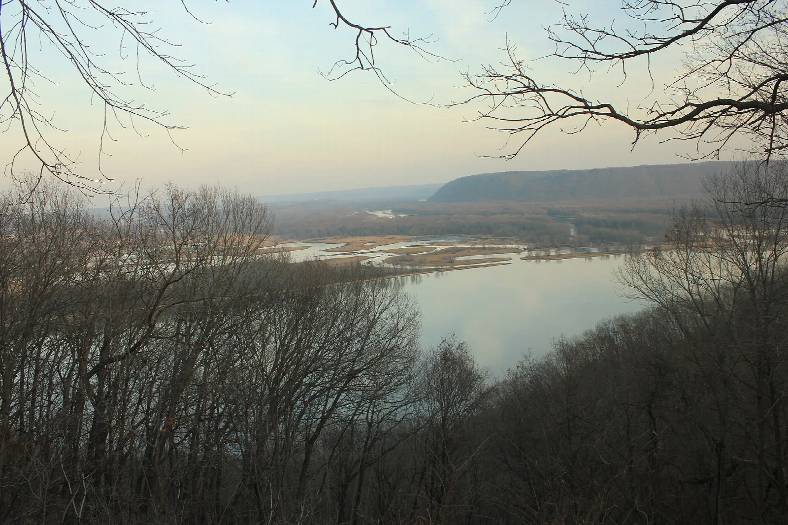 Wide river valley with a bluff on the far shore seen through bare branches