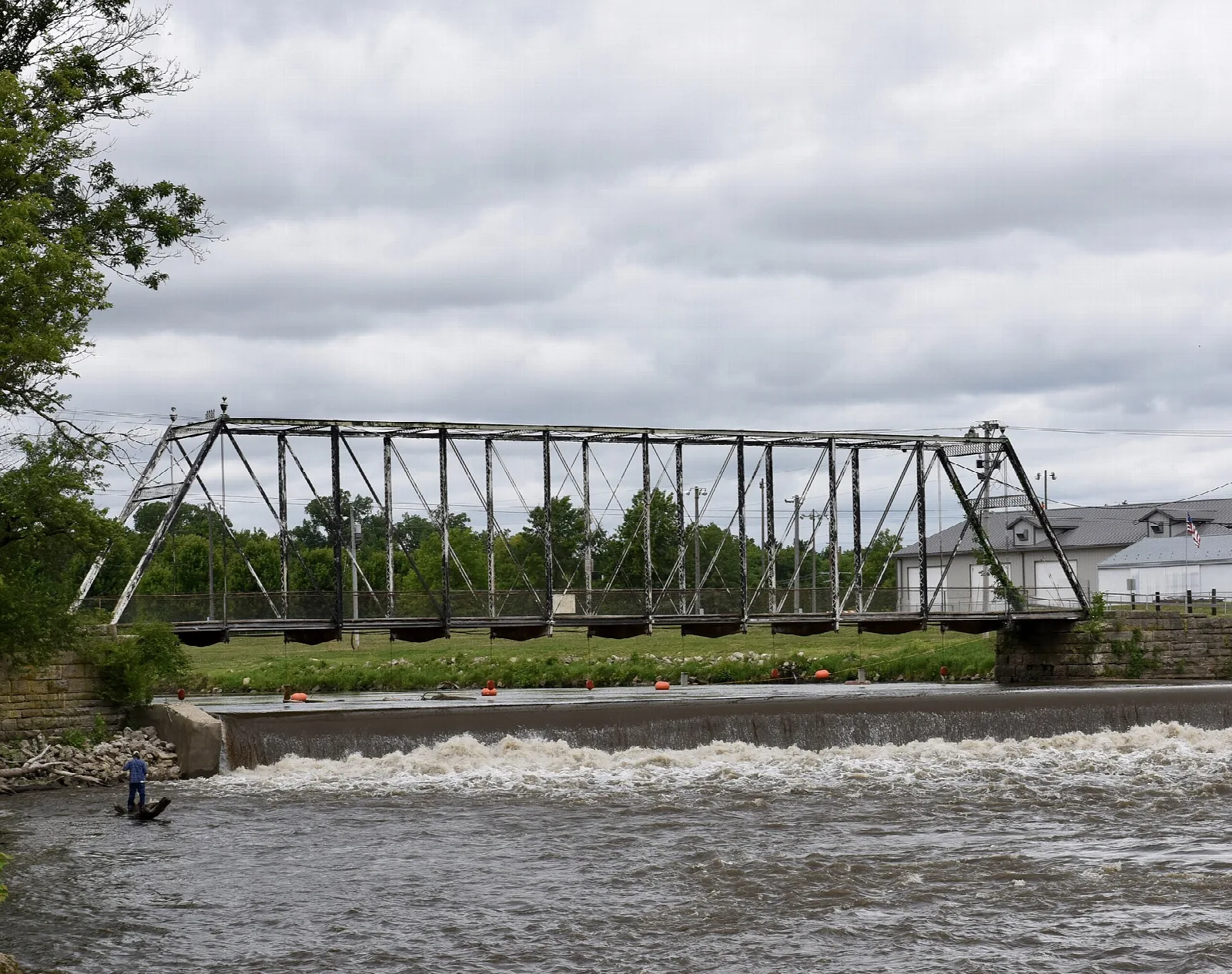Iron truss bridge over a river with a low dam and rapids below