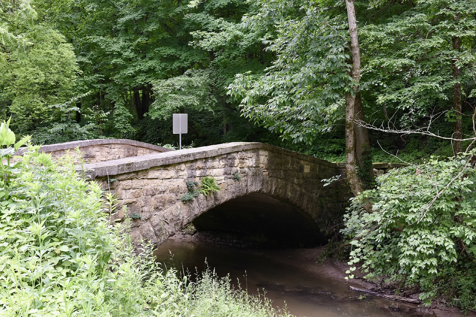 Old stone arch bridge over a small creek in green woods