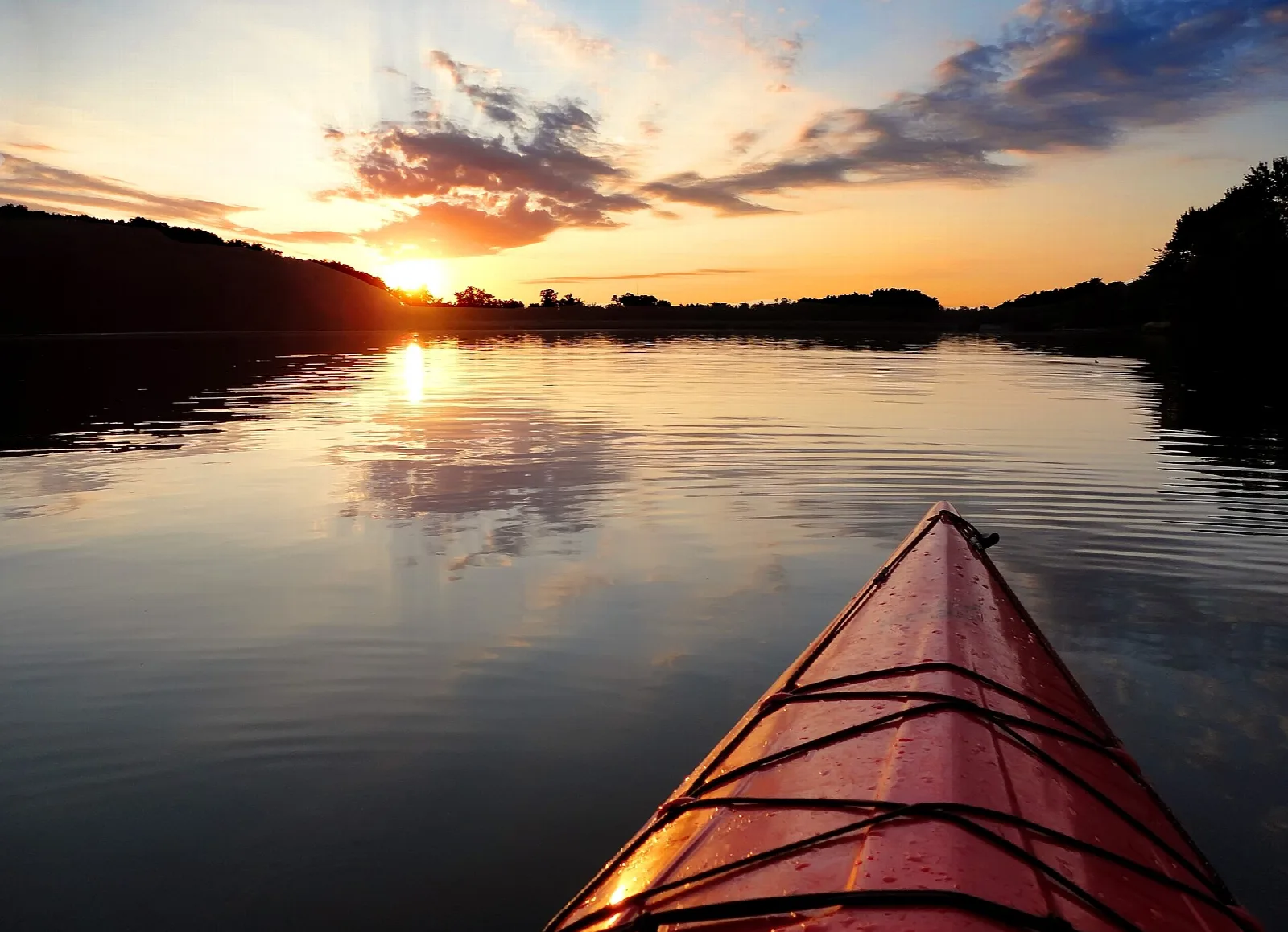 Red kayak bow on calm lake water at sunset