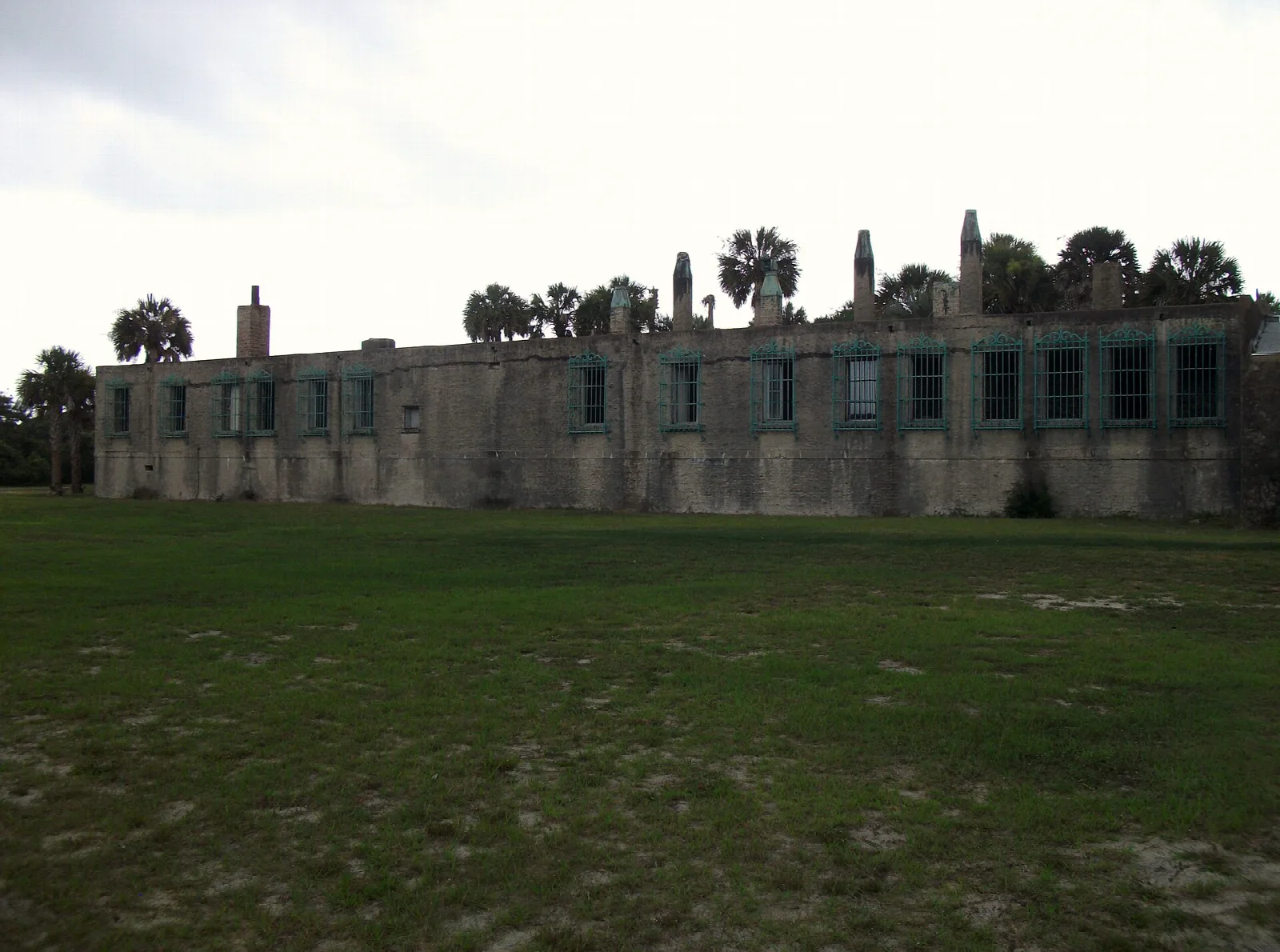 Long low stone building across a green lawn with palms behind