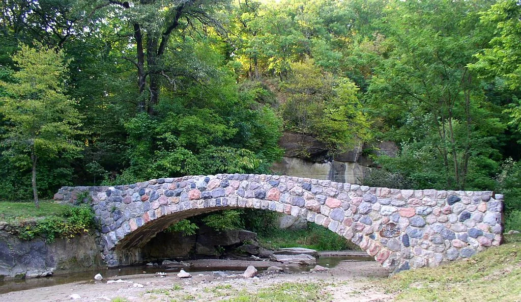 Stone arch bridge over a creek bed with trees behind