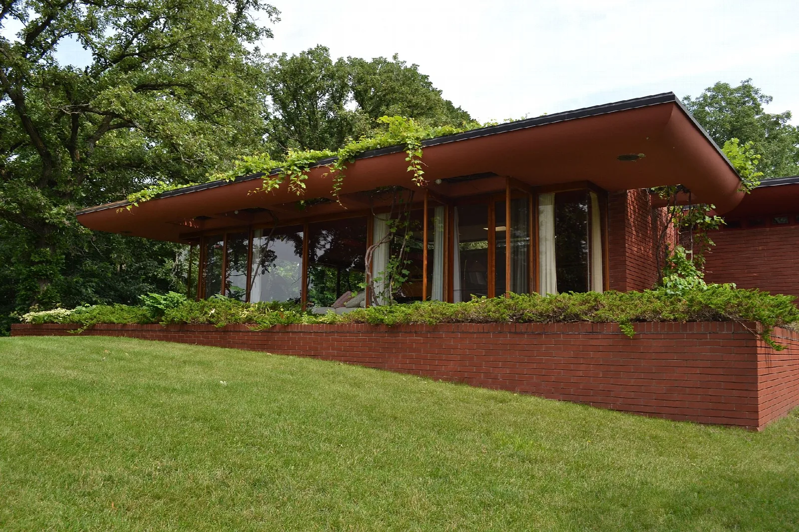 Brick house with a long flat roof and ivy over a green lawn under trees
