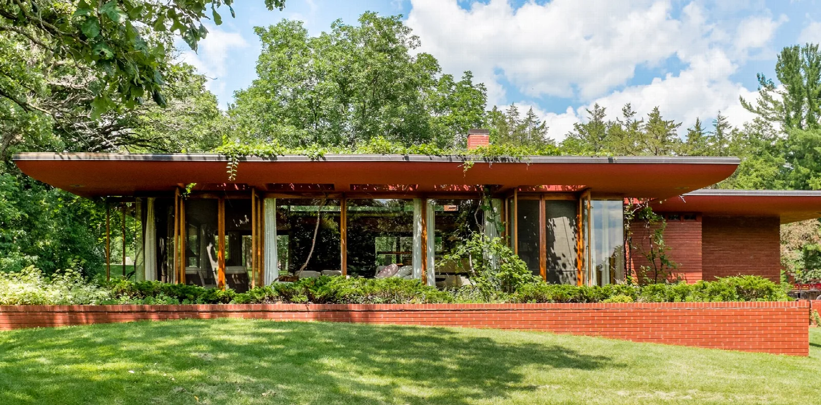 Low flat-roofed brick house with glass walls surrounded by trees and lawn