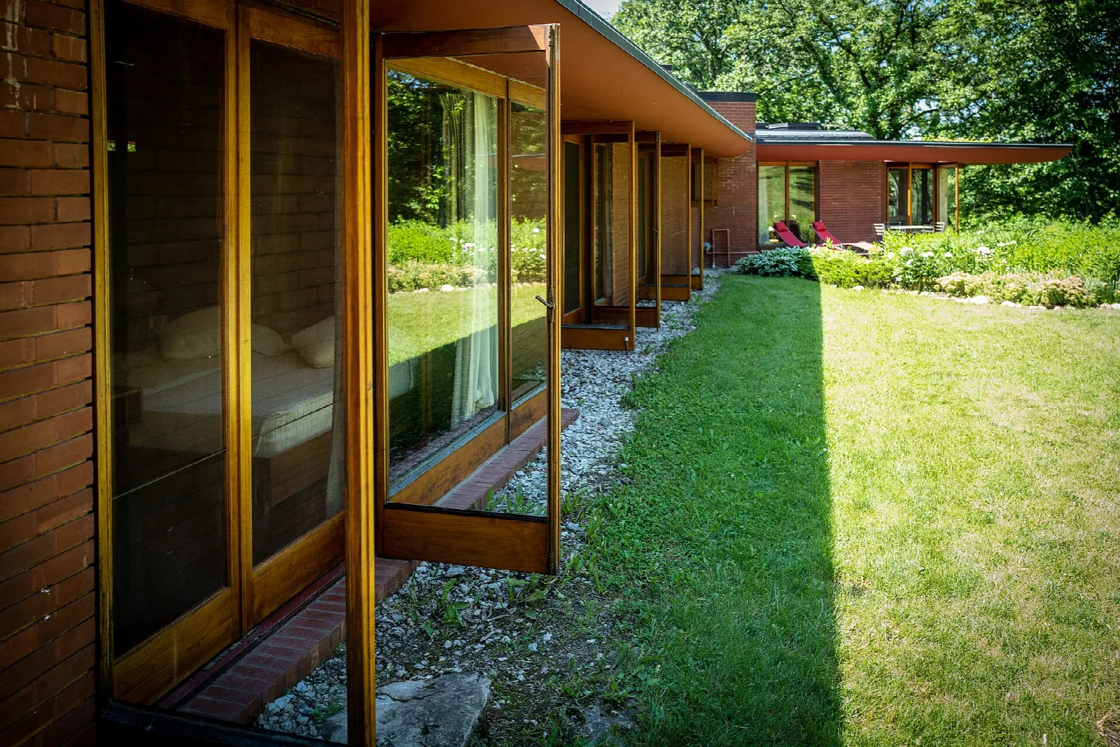Glass and wood wall of a brick house beside a gravel border and long lawn
