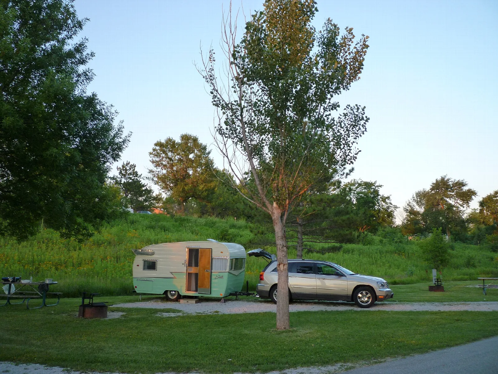 Camper trailer and a car parked at a grassy campsite with trees behind