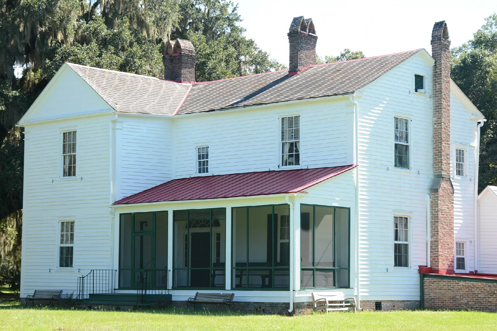 White two-story plantation house with a red porch roof under live oaks
