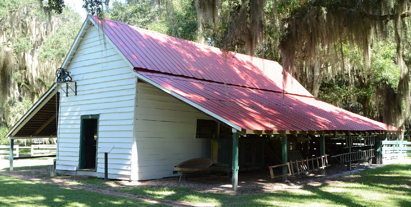White wooden barn with a long red metal roof on a lawn