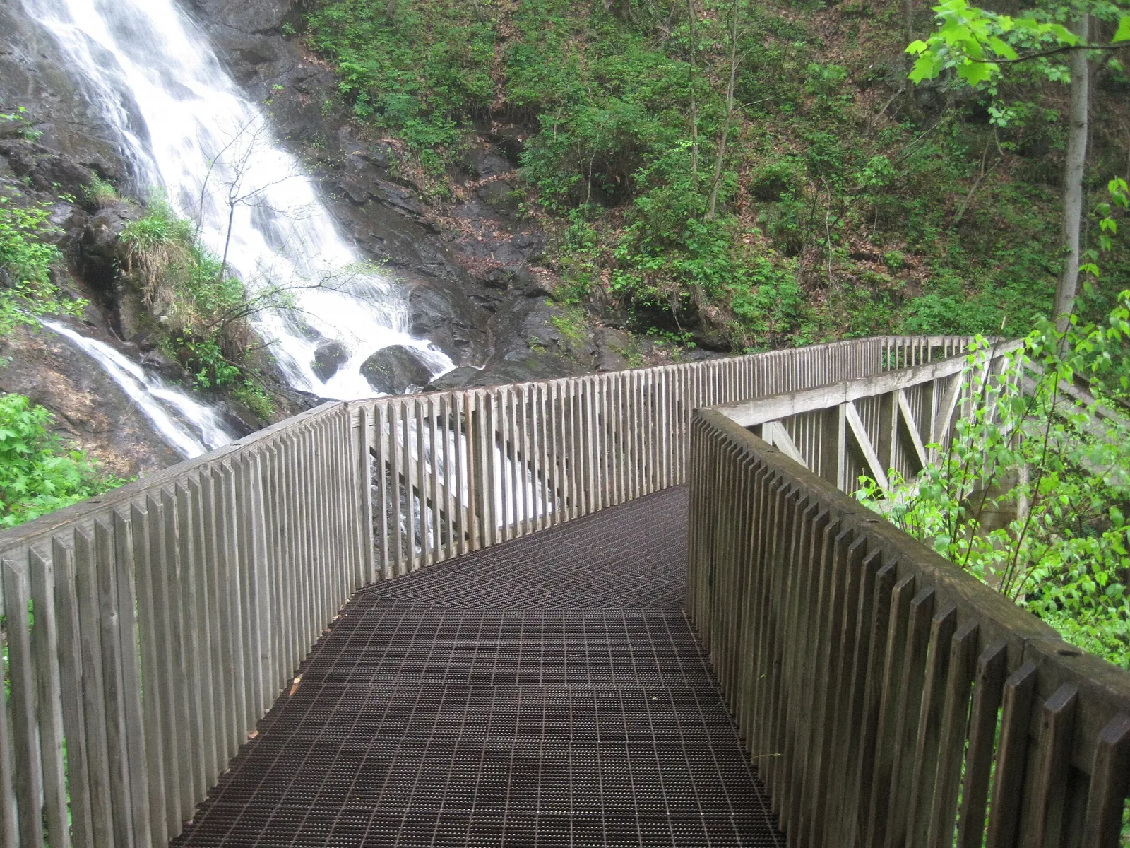 Wooden observation bridge crossing in front of a waterfall
