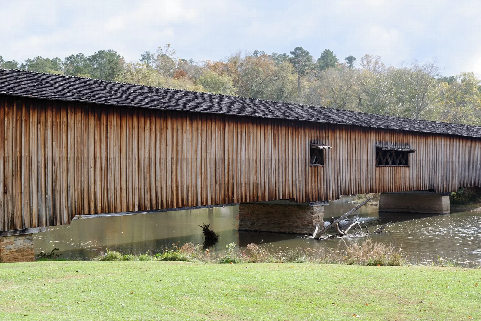 Long wooden covered bridge over a river beside a green lawn