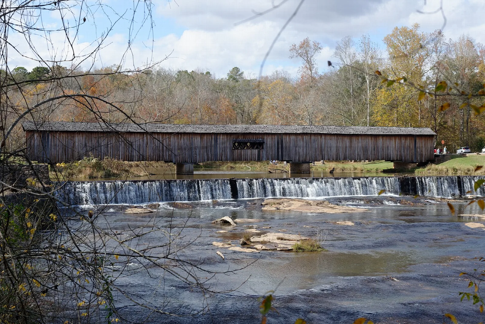 Covered bridge behind a low dam and rocky river