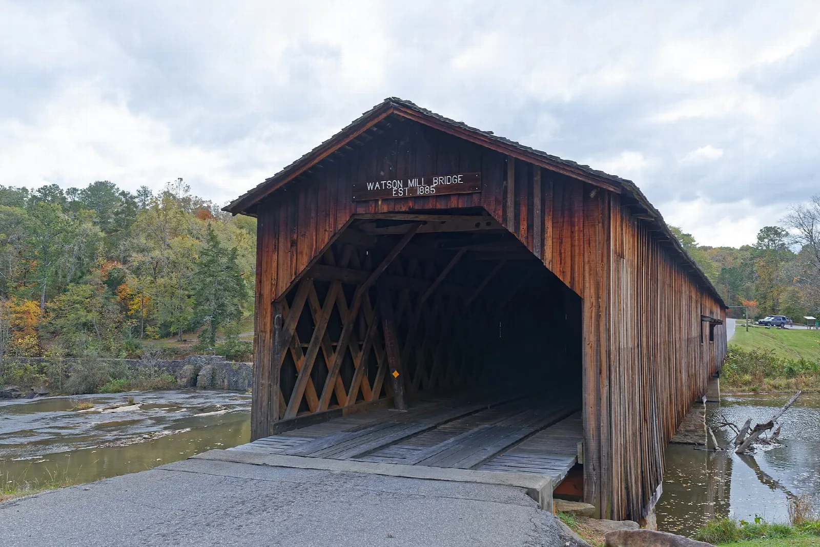 End of a wooden covered bridge with lattice sides and a paved road