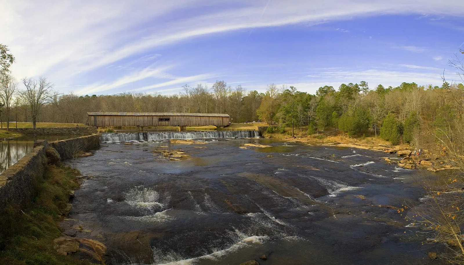 Covered bridge in the distance across a wide, rocky river under a streaked sky