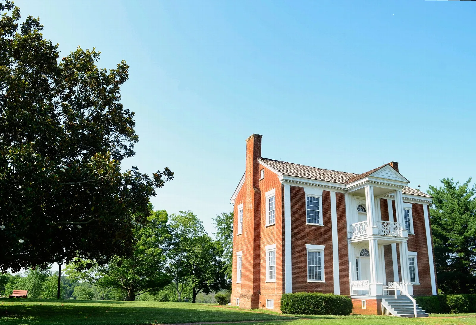 Brick house with a white porch seen across a lawn under blue sky