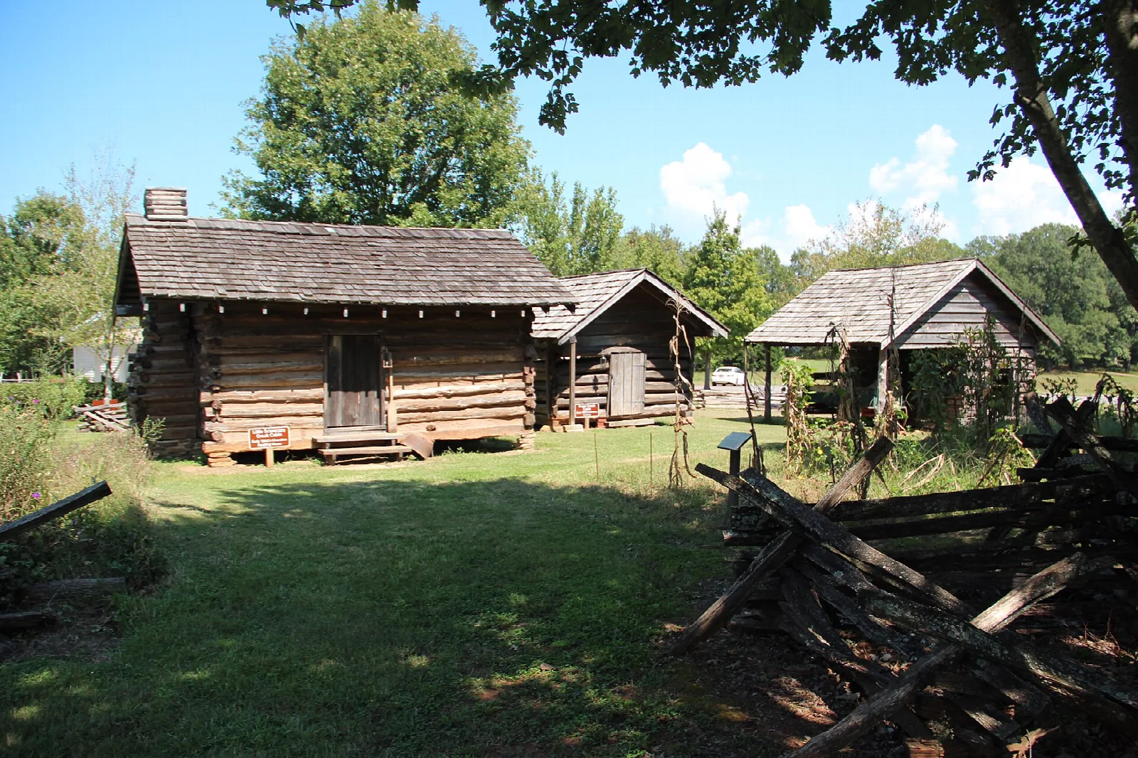 Log cabins in a grassy yard with a split-rail fence