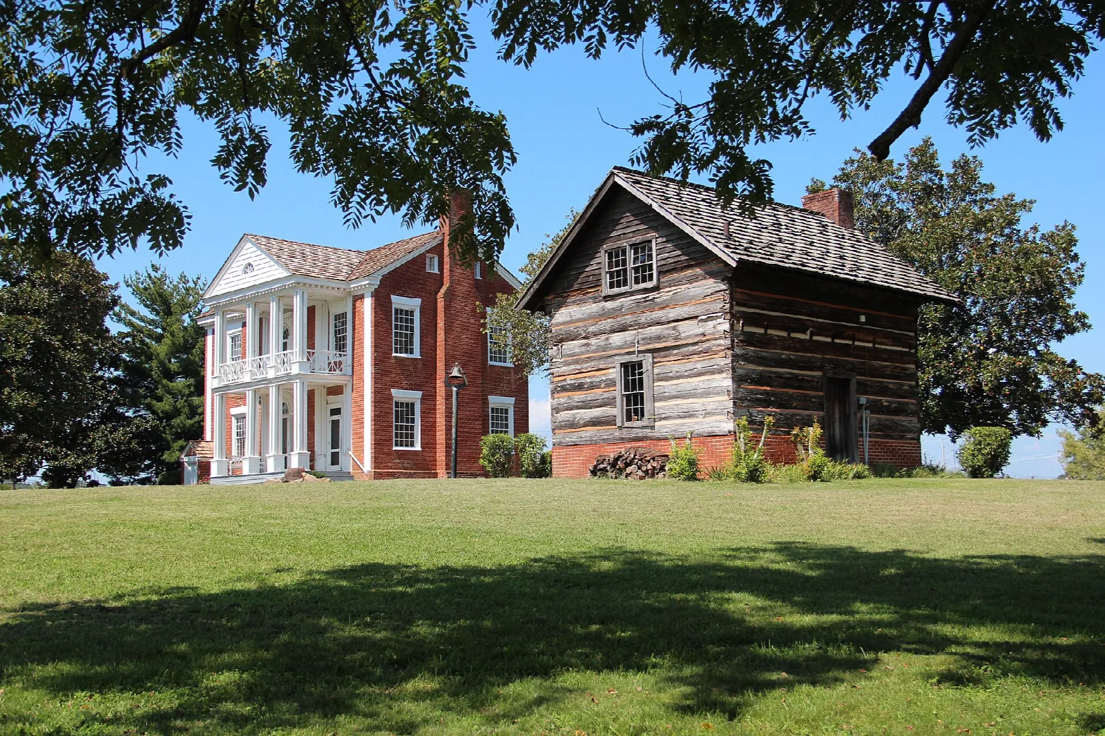 Brick house beside a log building with a lawn in front
