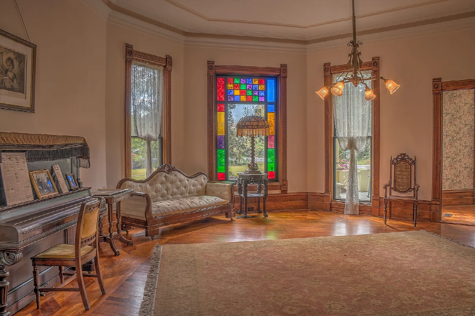 Parlor with a stained glass window, piano and sofa on a wood floor