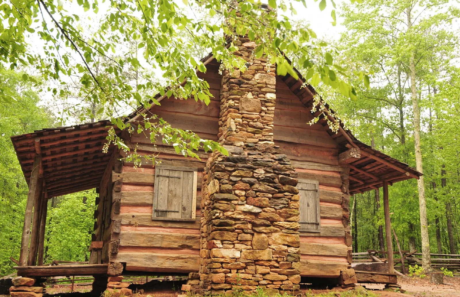 Log cabin with a stone chimney and covered porch in green woods