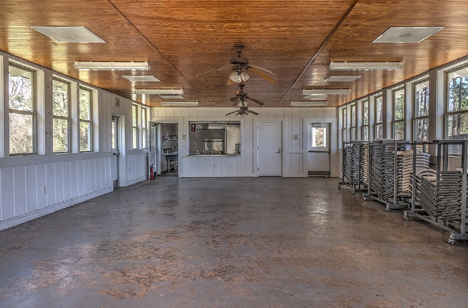 Large open room with a wood ceiling, windows along the walls and a concrete floor