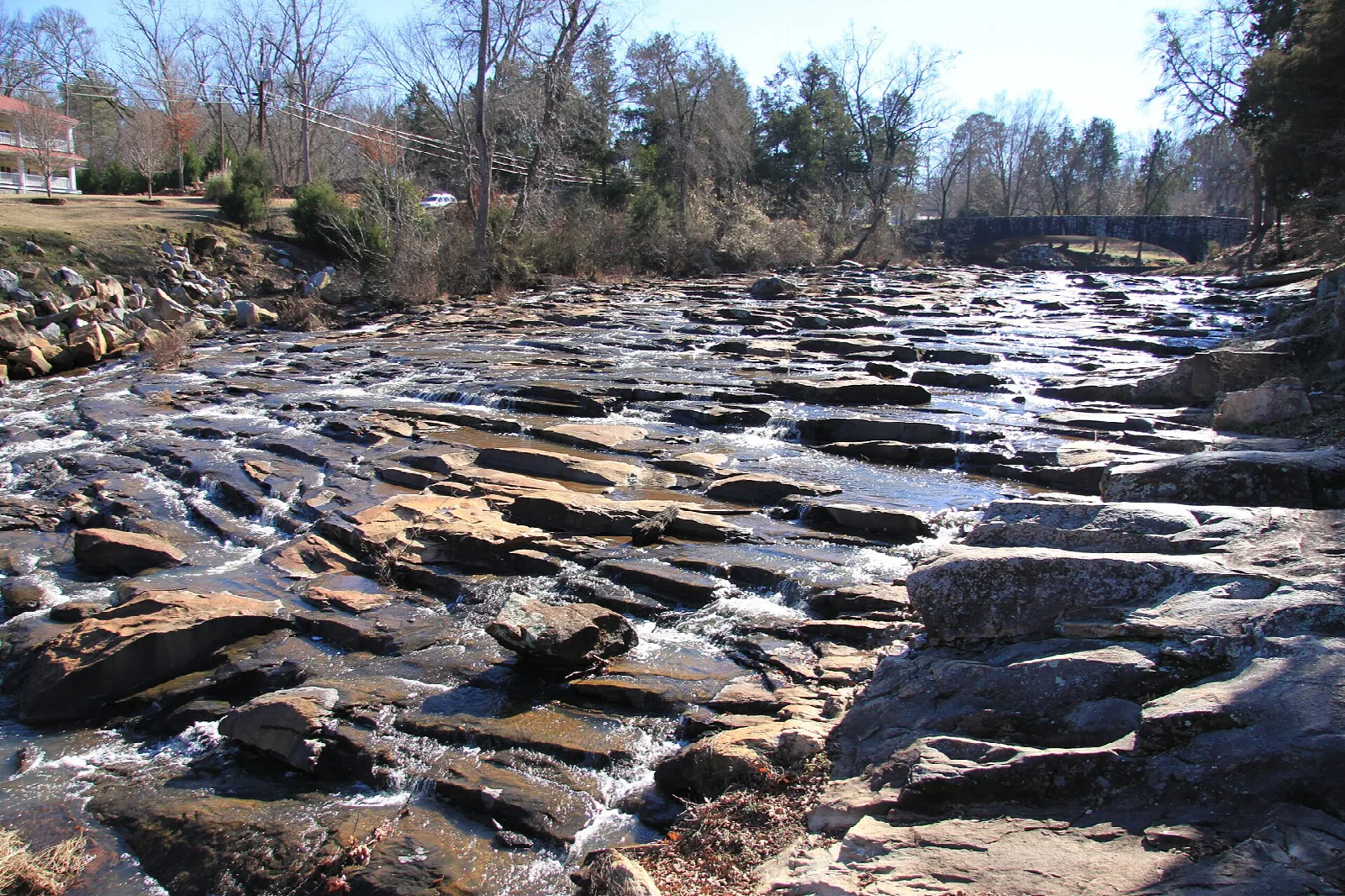 Shallow creek tumbling over flat rock ledges between bare trees