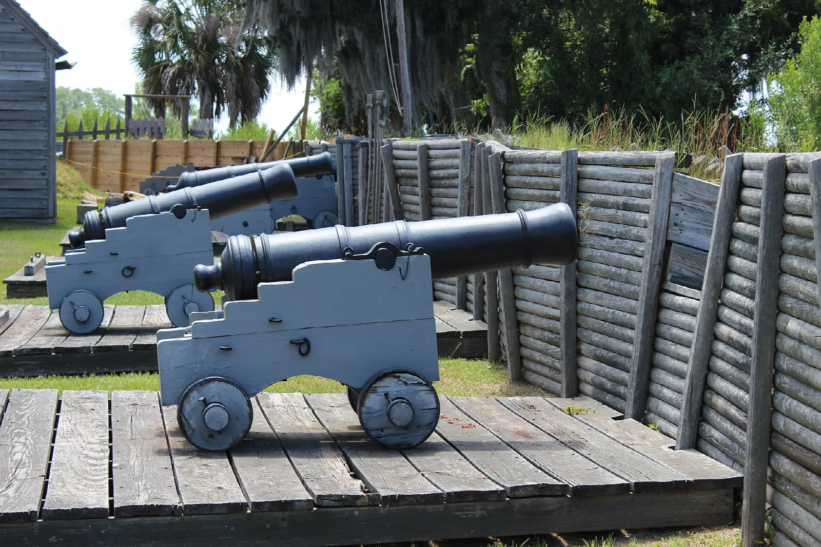 Two black cannons on a wooden platform behind a log palisade