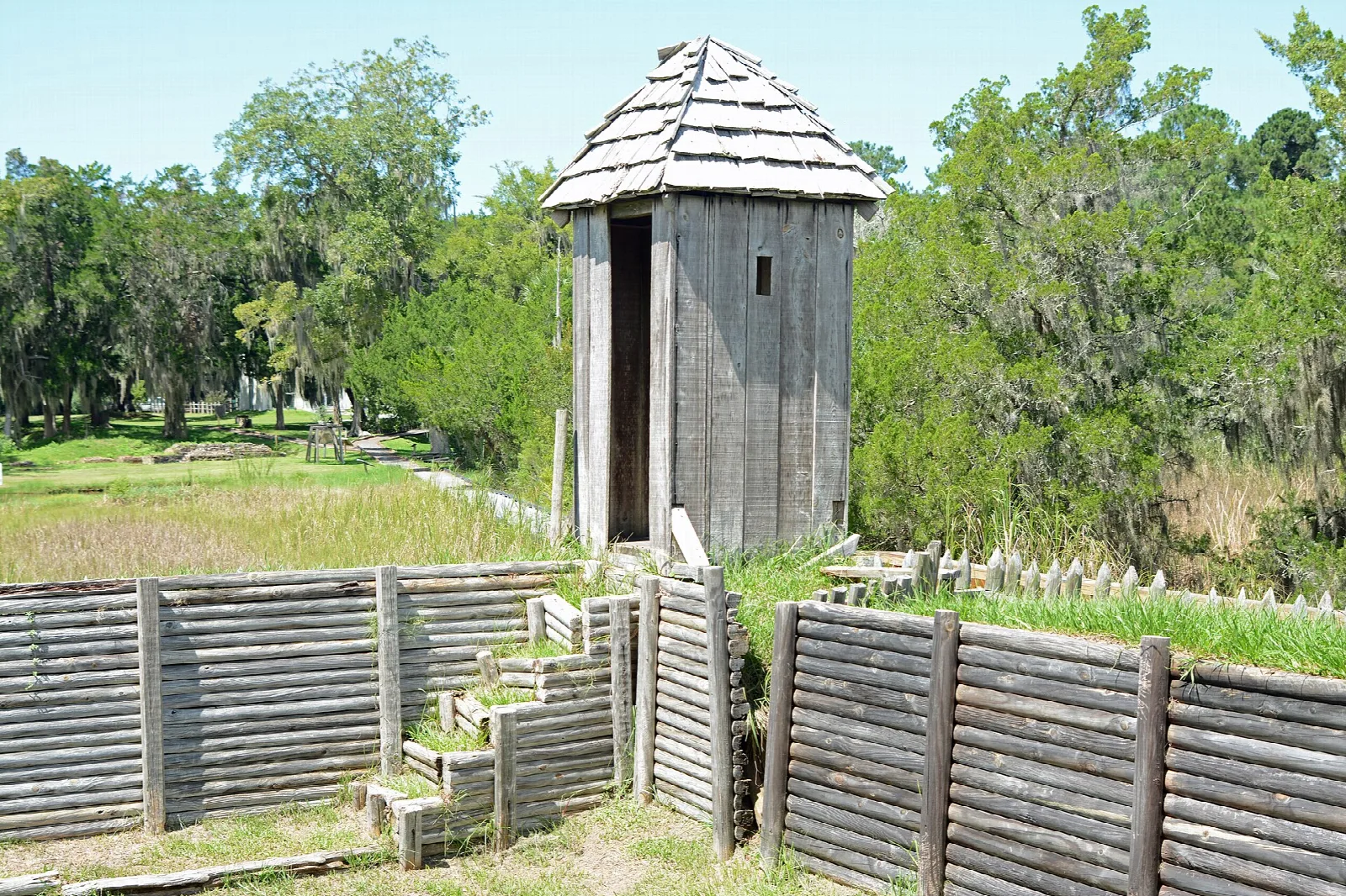 Wooden sentry tower with a shingle roof beside a stepped log palisade