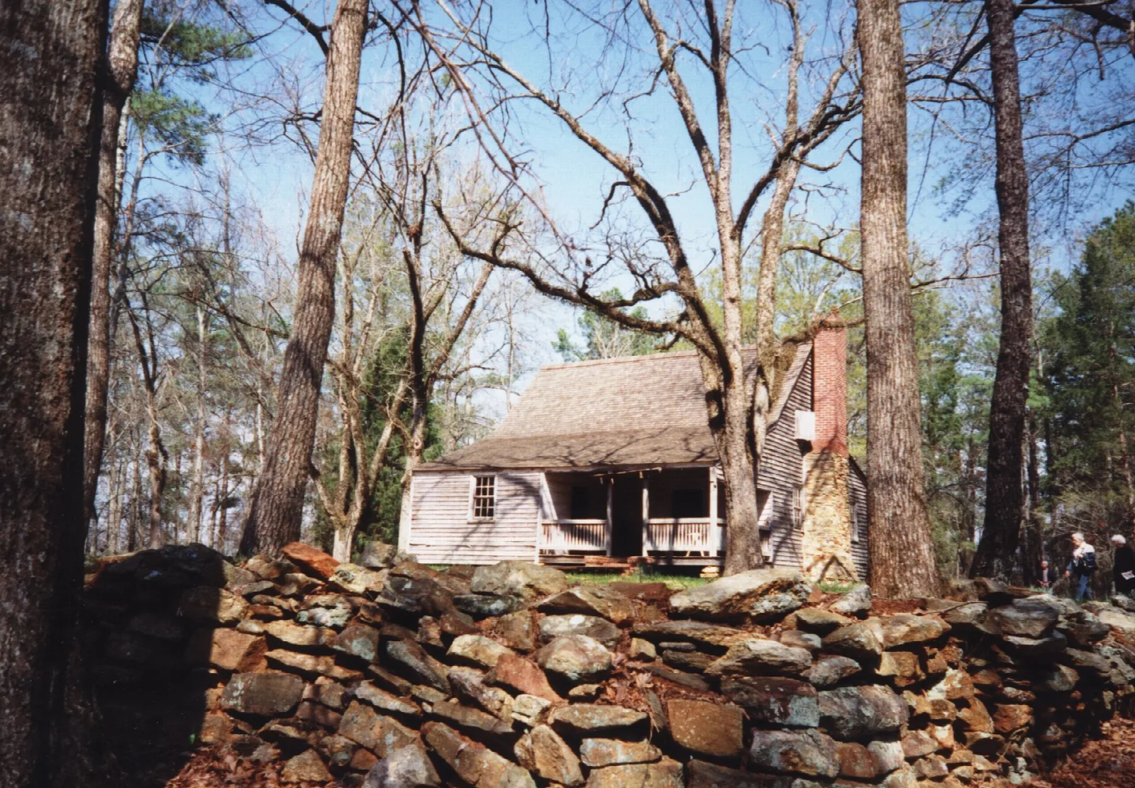 Small wooden house seen over a rock wall among bare trees