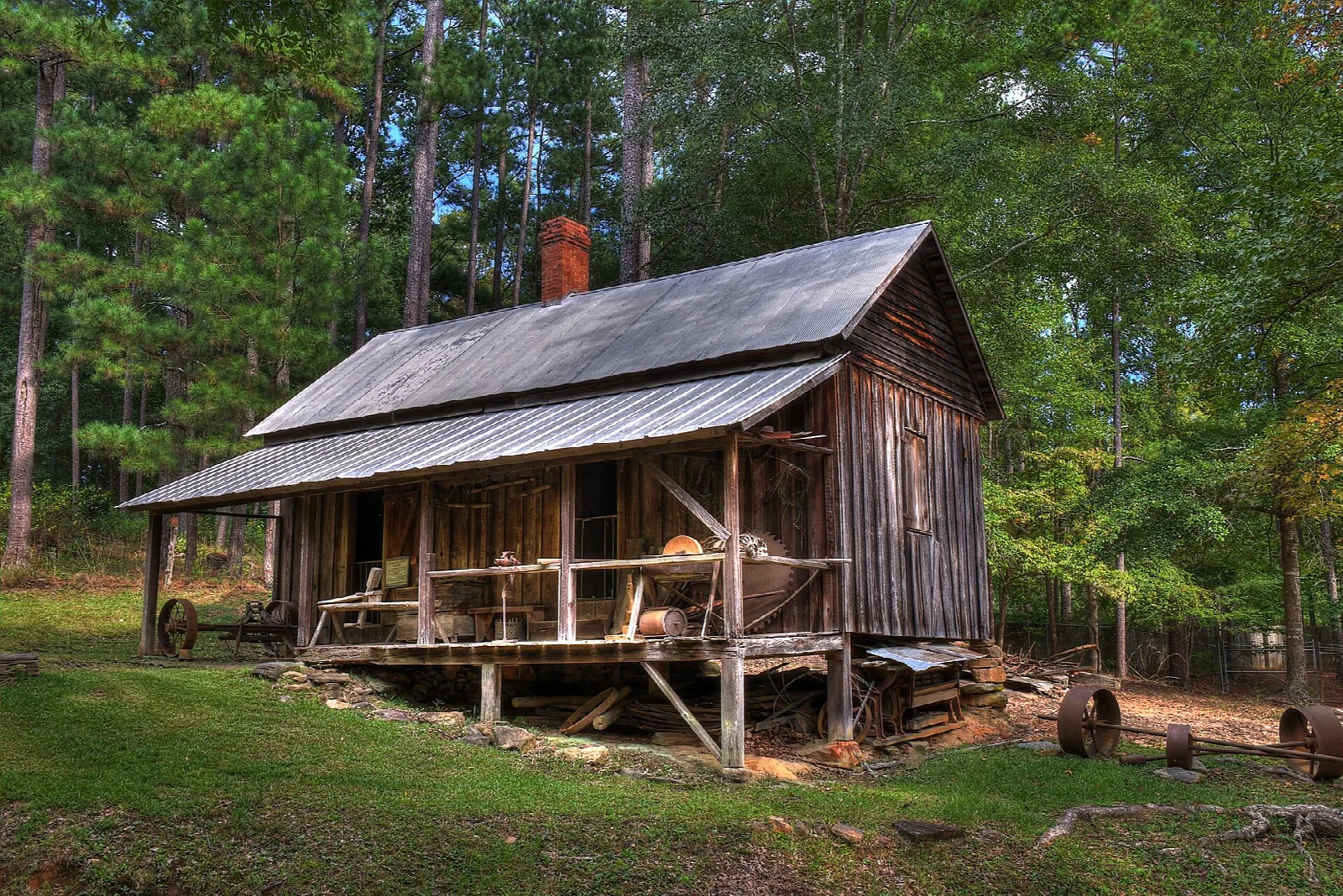 Weathered wooden workshop with a metal roof and open porch in a forest clearing
