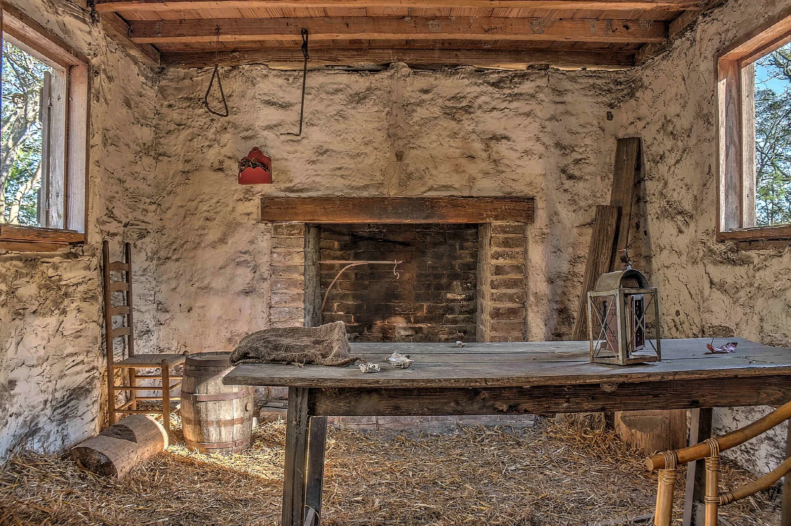 Rustic room with a stone fireplace, a wooden table and straw on the floor