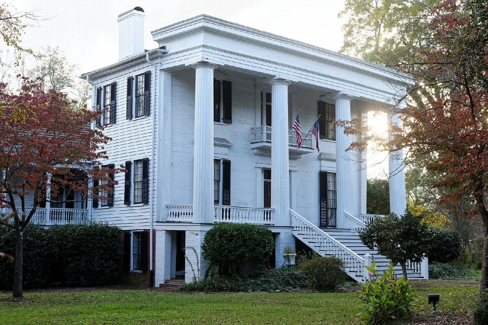 White columned house seen from the side with autumn trees around it