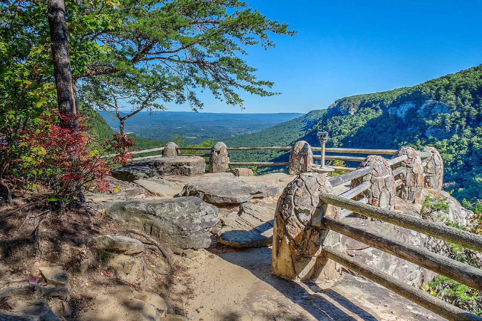 Stone-railed viewing platform above a forested canyon with blue sky