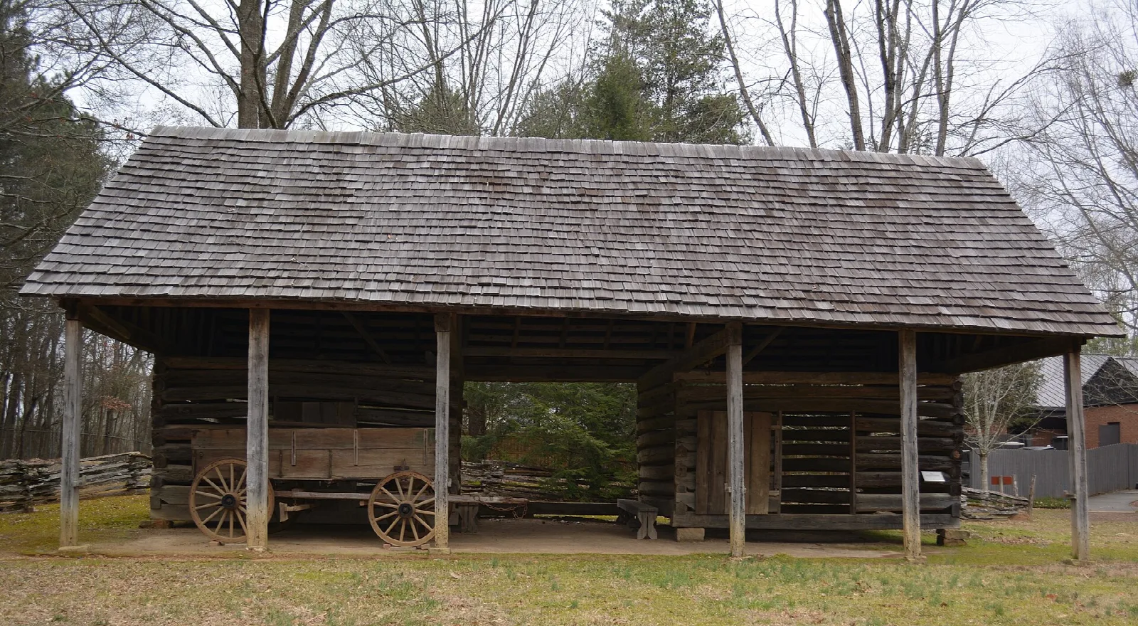 Long open log barn with a shingle roof and a wagon inside