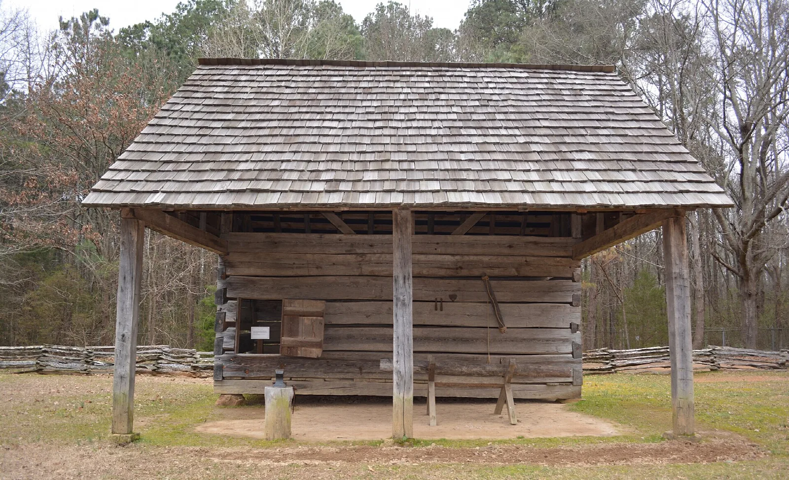 Small log corn crib with a wide shingle roof on a grassy field