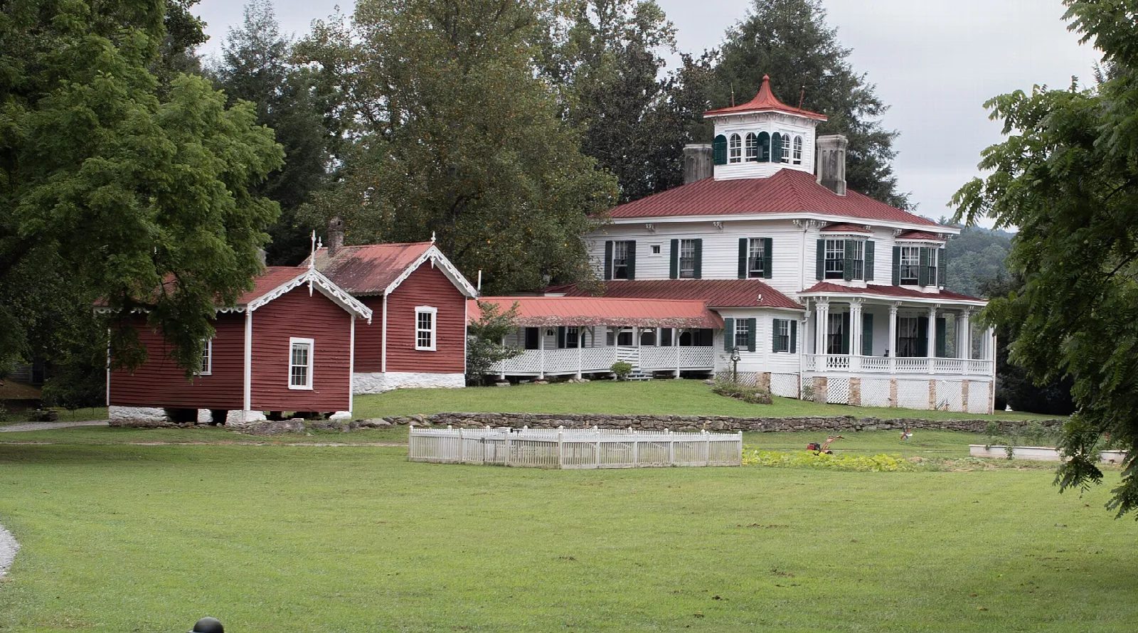 White Italianate mansion with a cupola beside a red barn on a green lawn