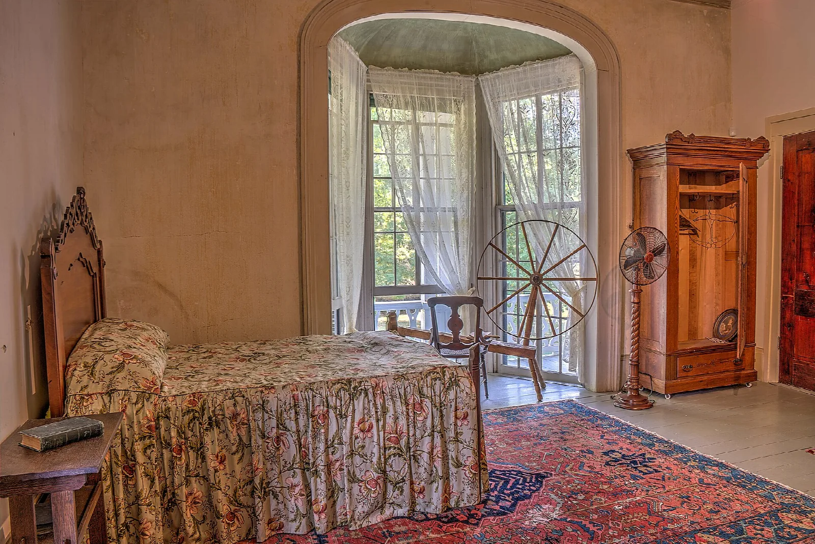 Bedroom with a floral bedspread, spinning wheel and tall window