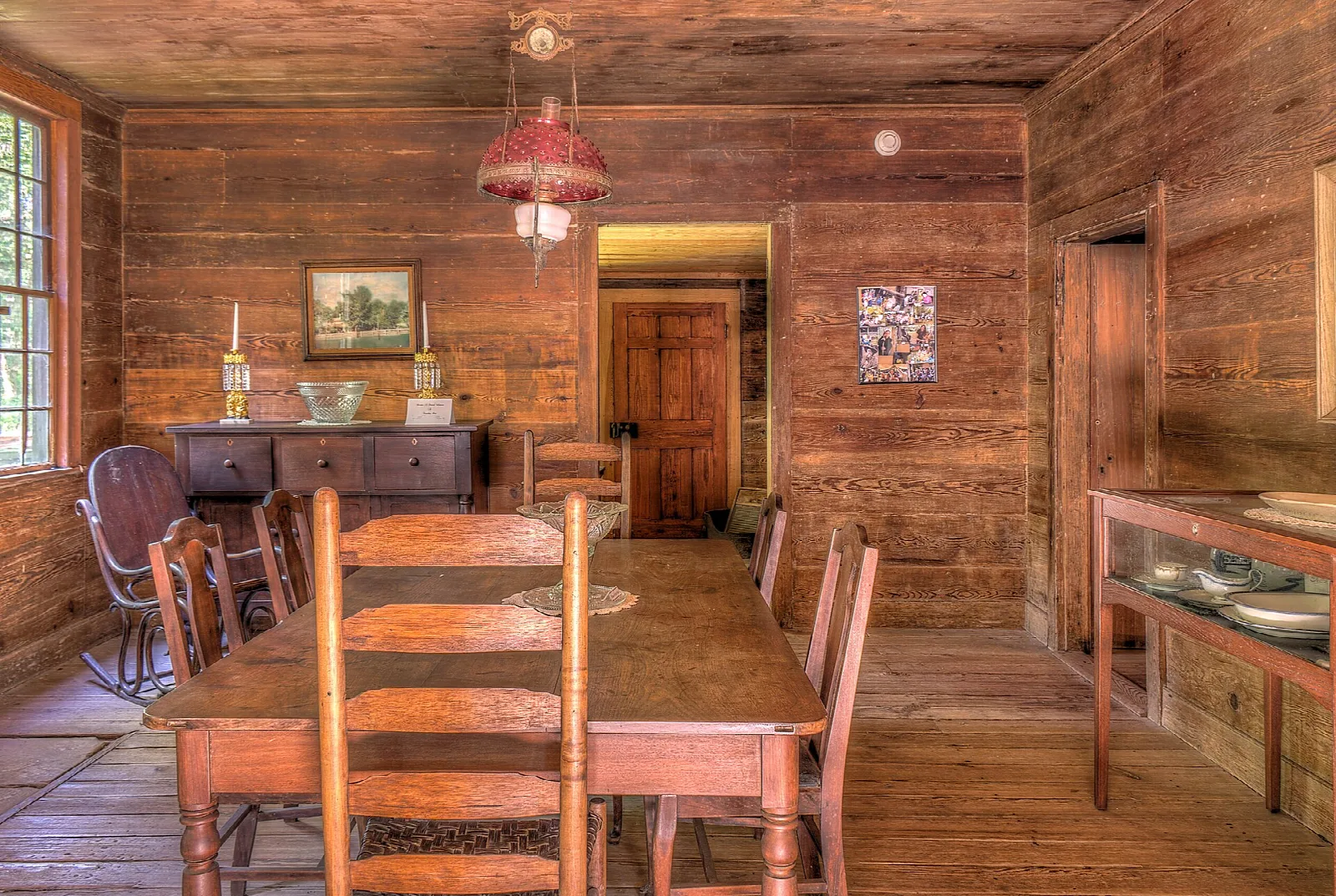 Wooden dining room with a long table, ladder-back chairs and a hanging red lamp