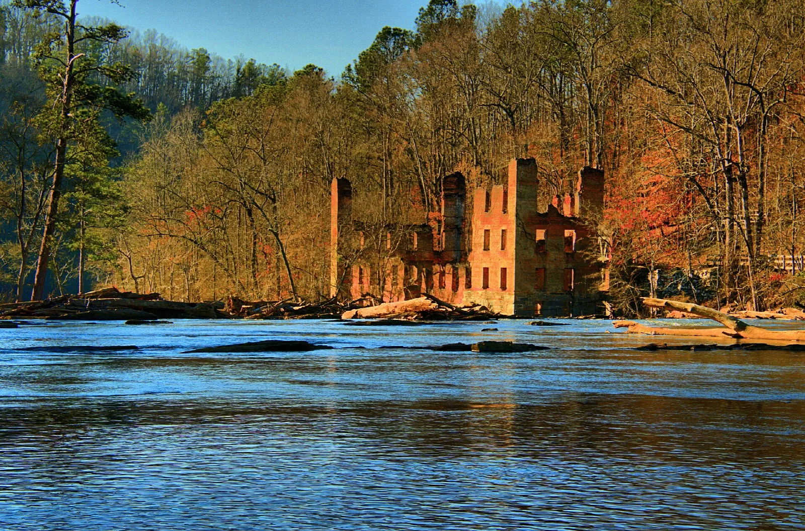 Brick mill ruins in autumn woods seen across a river at sunset