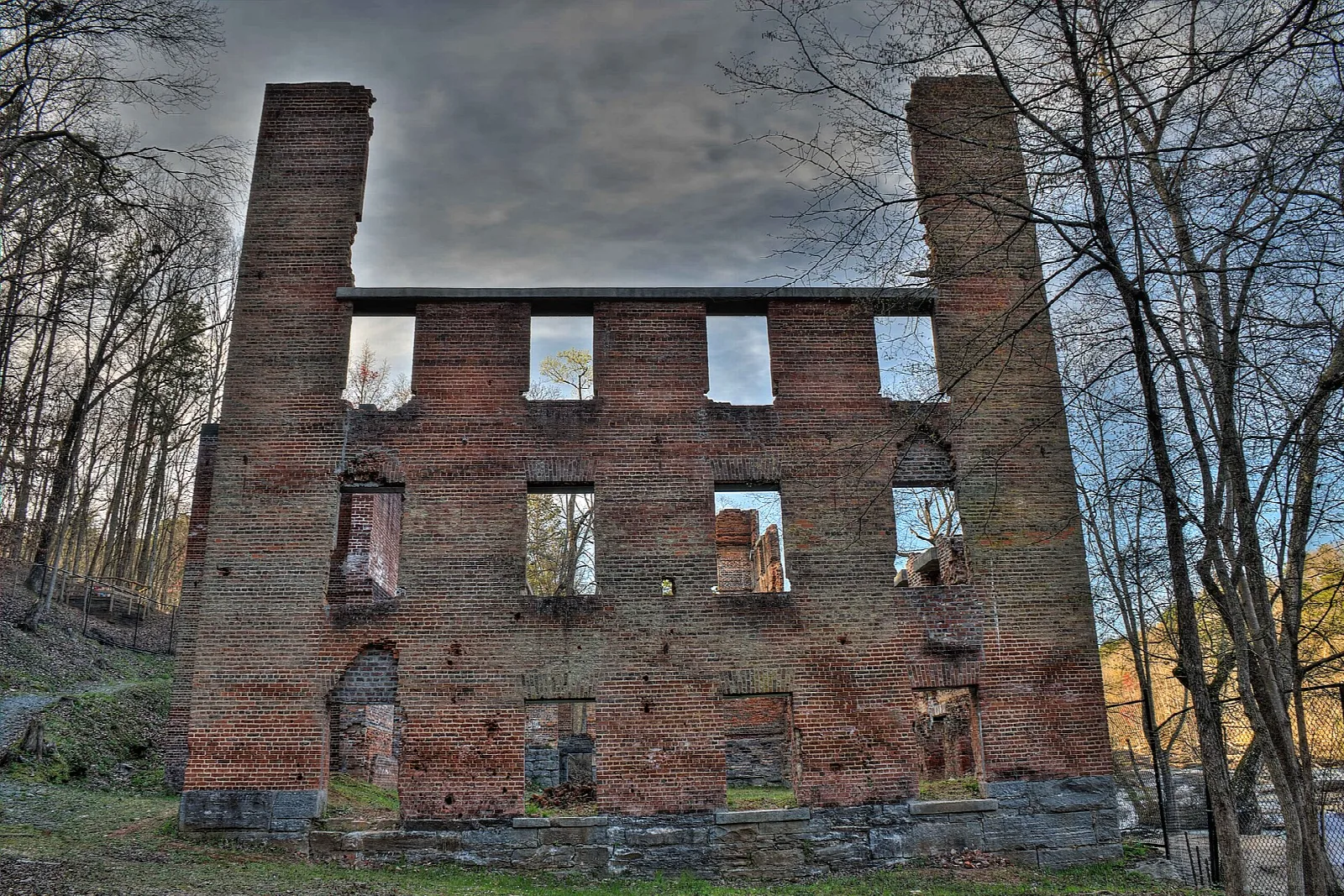 Tall brick mill ruin with chimneys and empty window openings under a gray sky