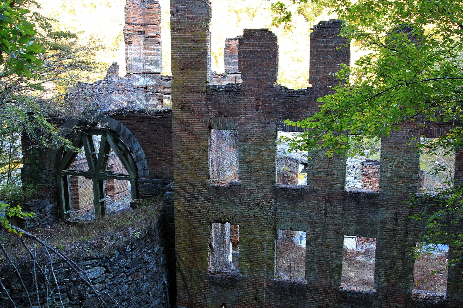 Brick textile mill ruins with a water wheel frame, framed by trees