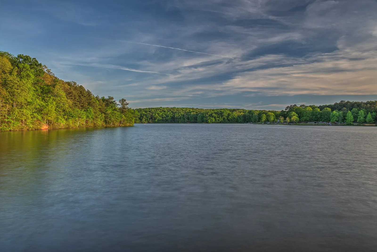 Calm reservoir with a tree-lined shore under a blue sky
