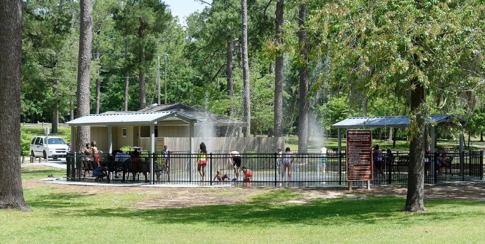 Splash pad with covered seating among pine trees and a lawn