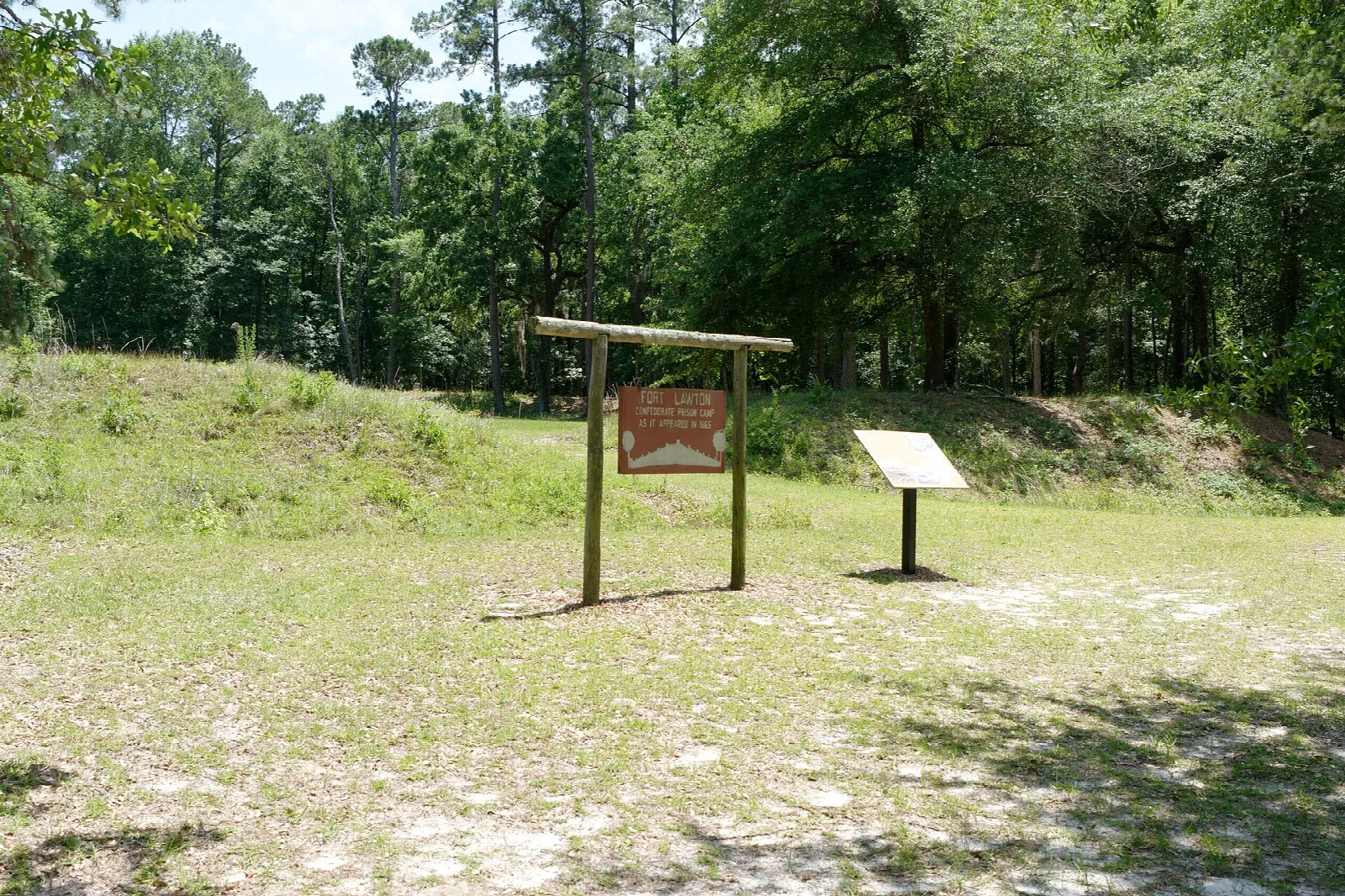 Grassy earthen breastworks and two signs in an open pine clearing