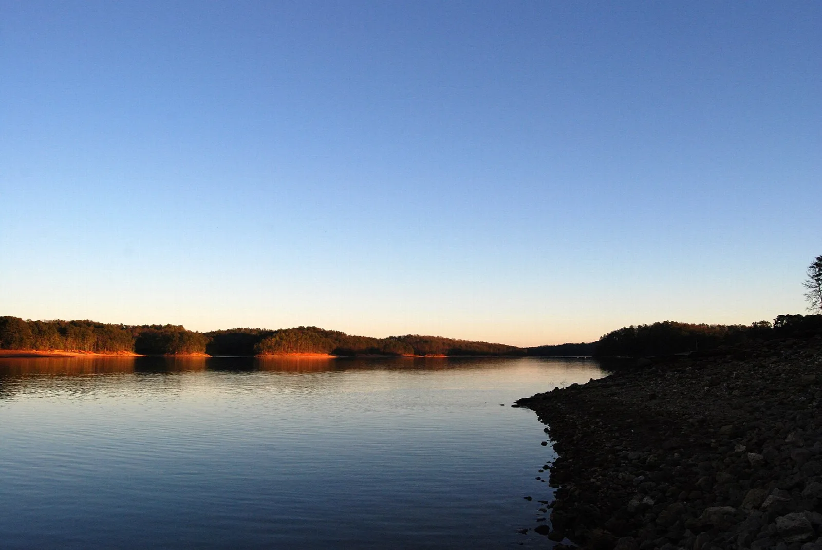 Lake at dusk with a tree-lined shore and clear sky