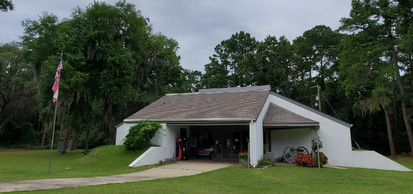 Low white building with a flag and cannons among trees